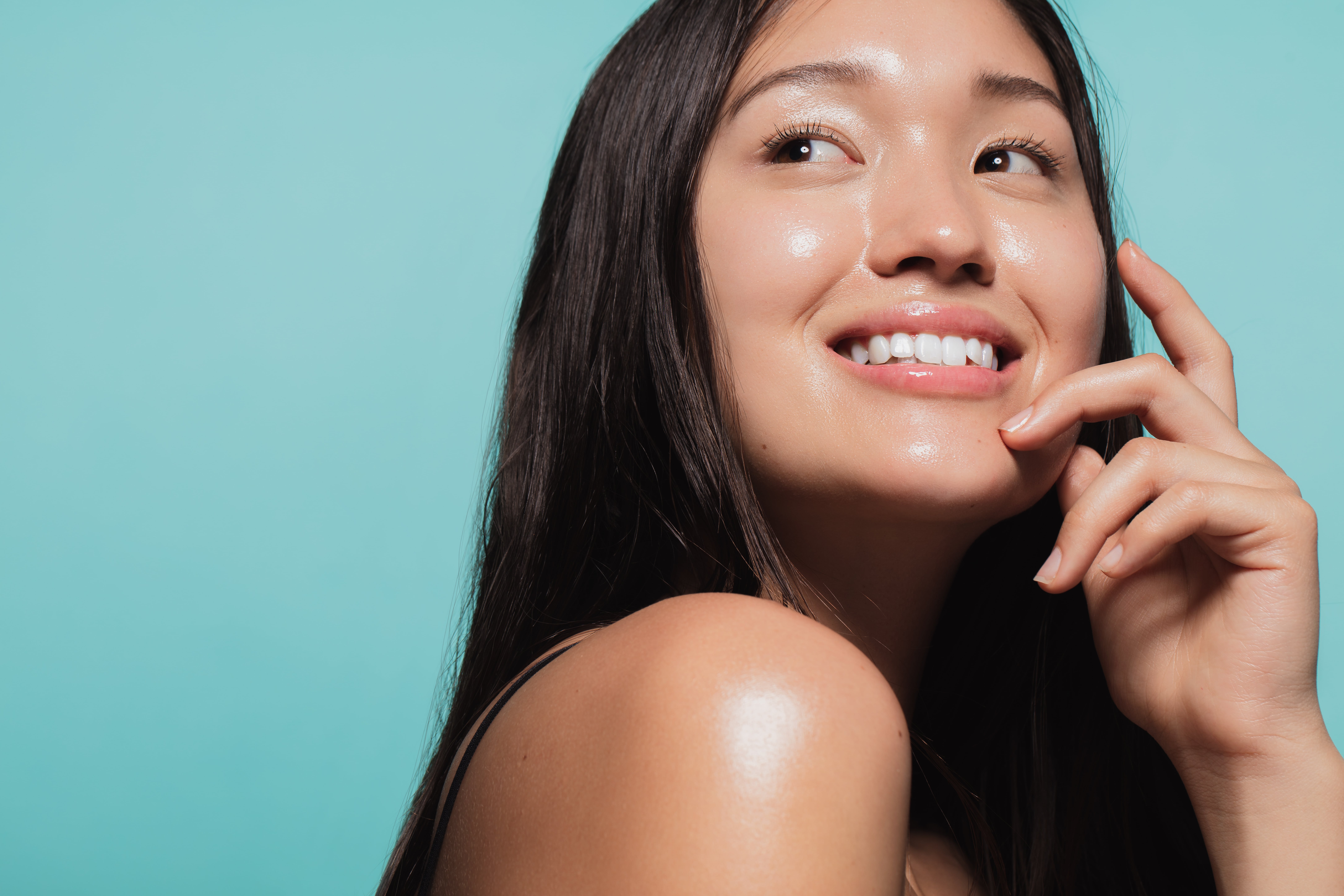 Woman admiring how her face looks after using products with actives against a solid blue background