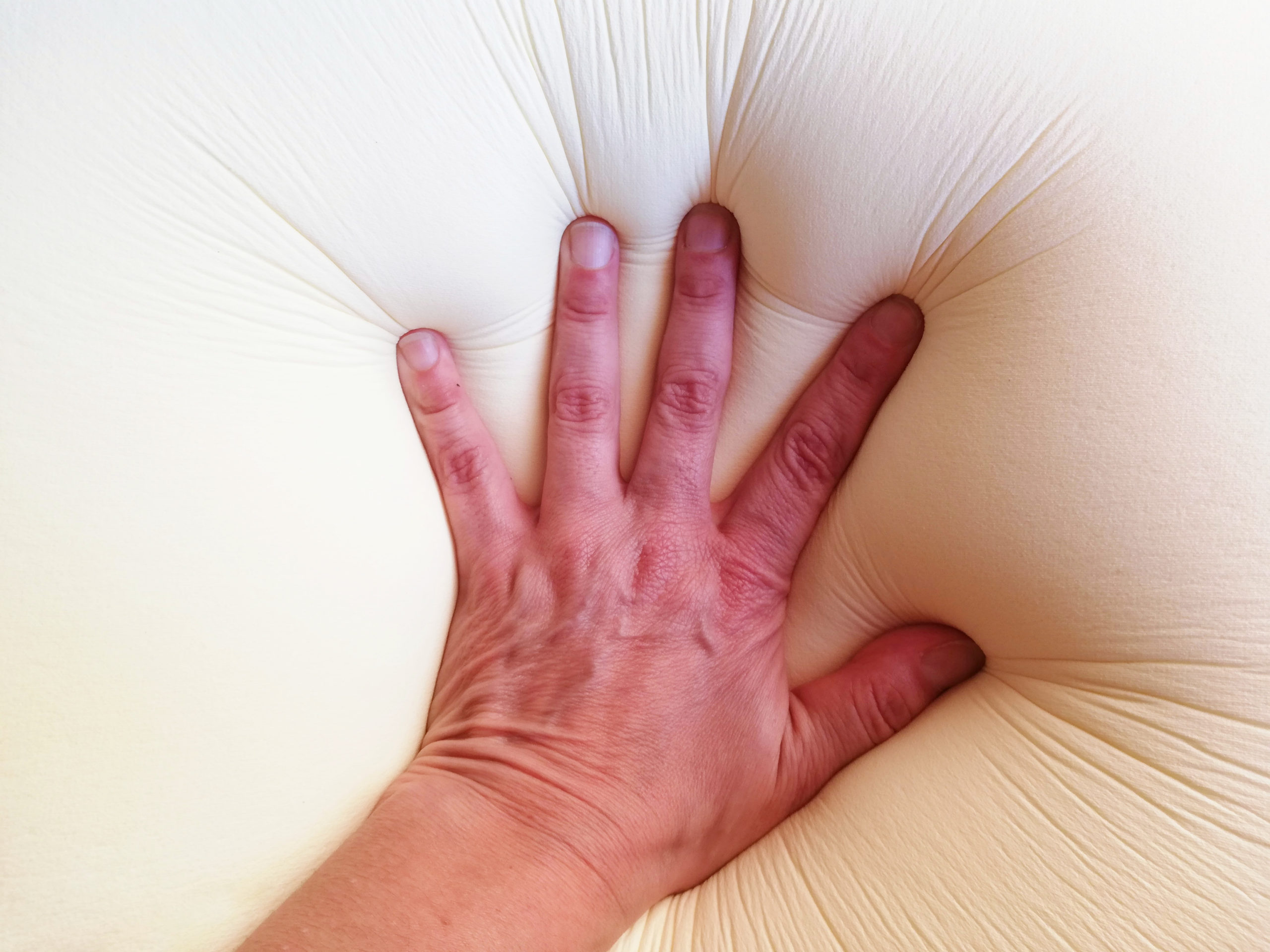 Sinking hand on a white memory foam pillow.