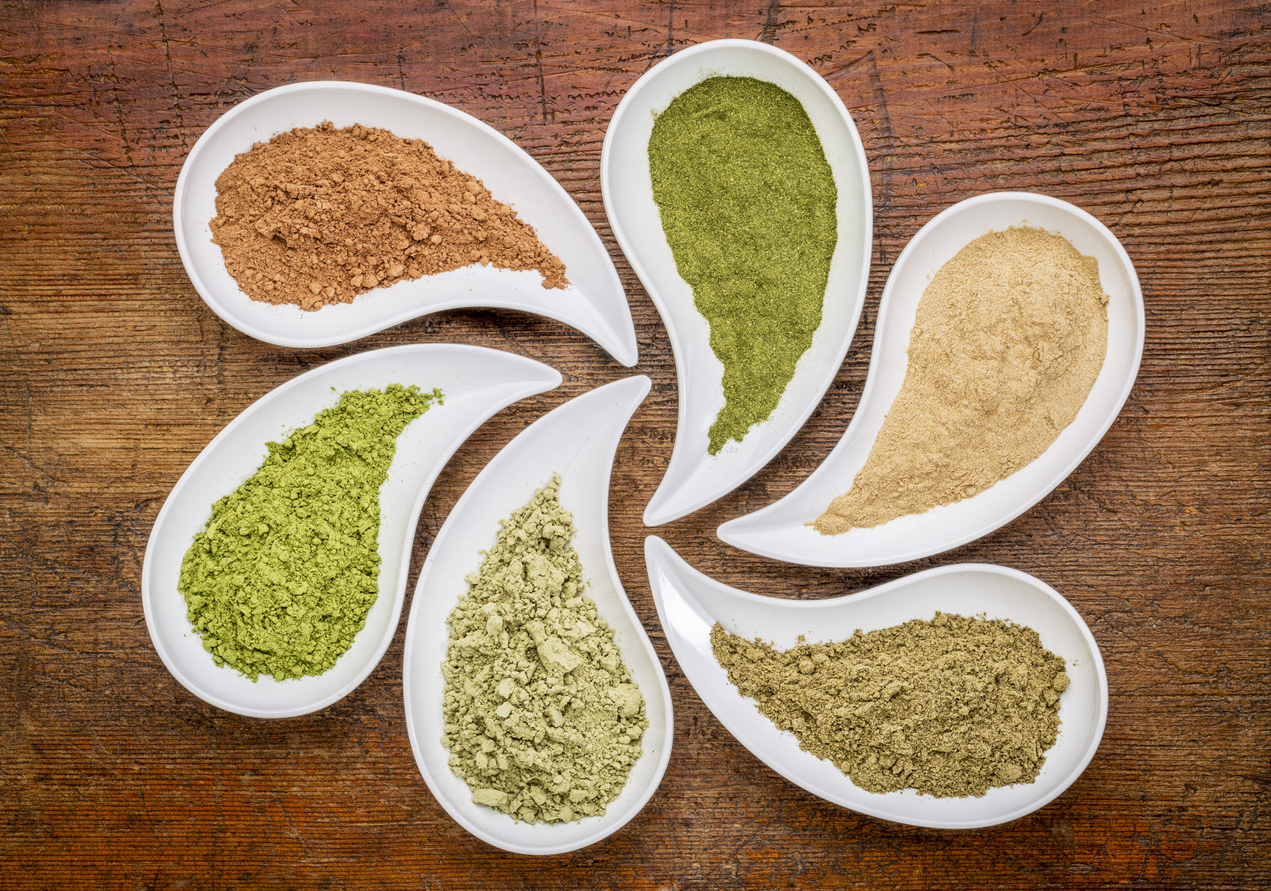 white bowls filled with different colored powders and botanical ingredients on a wooden table