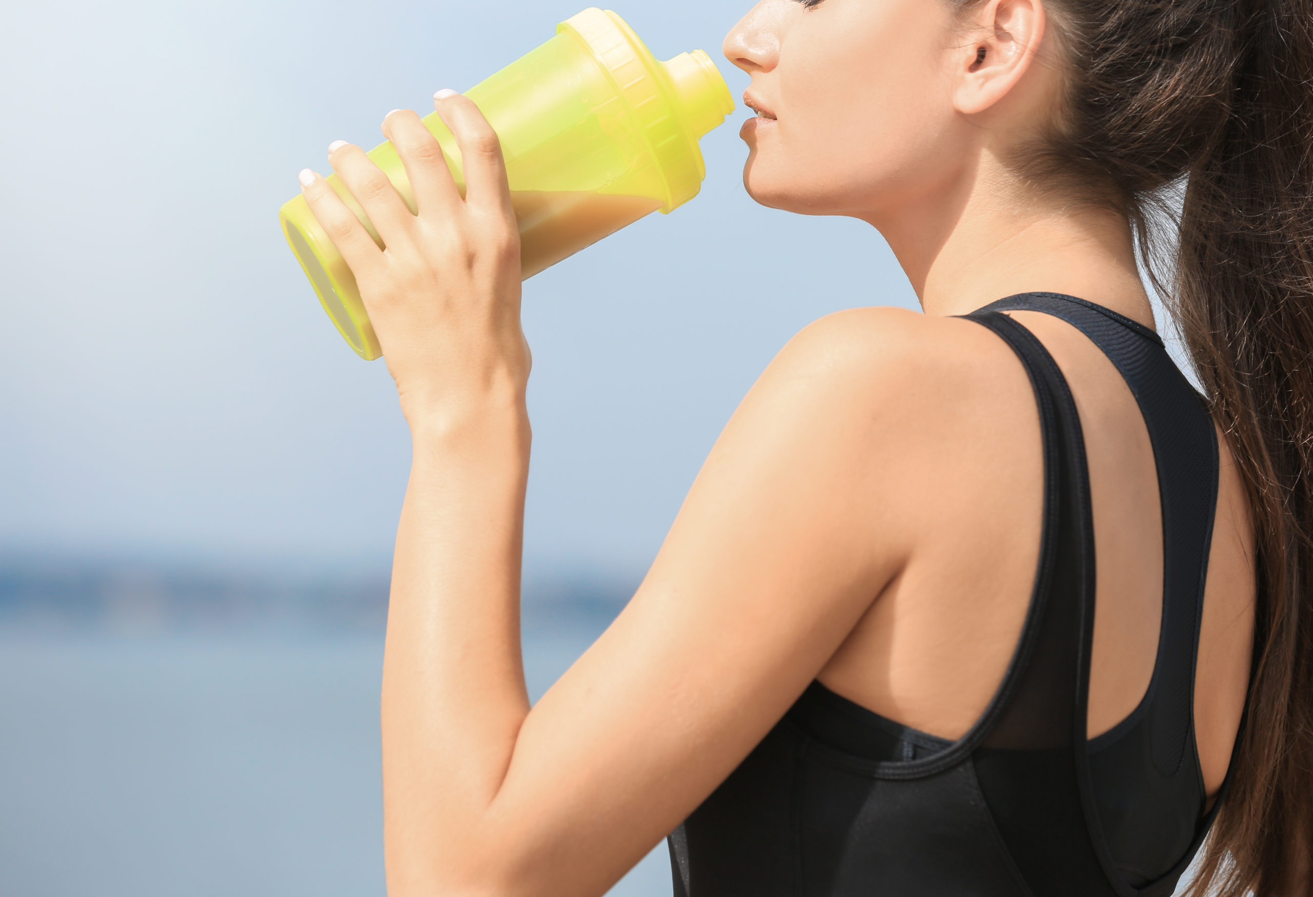 a woman in a black tank top drinks from a yellow shaker