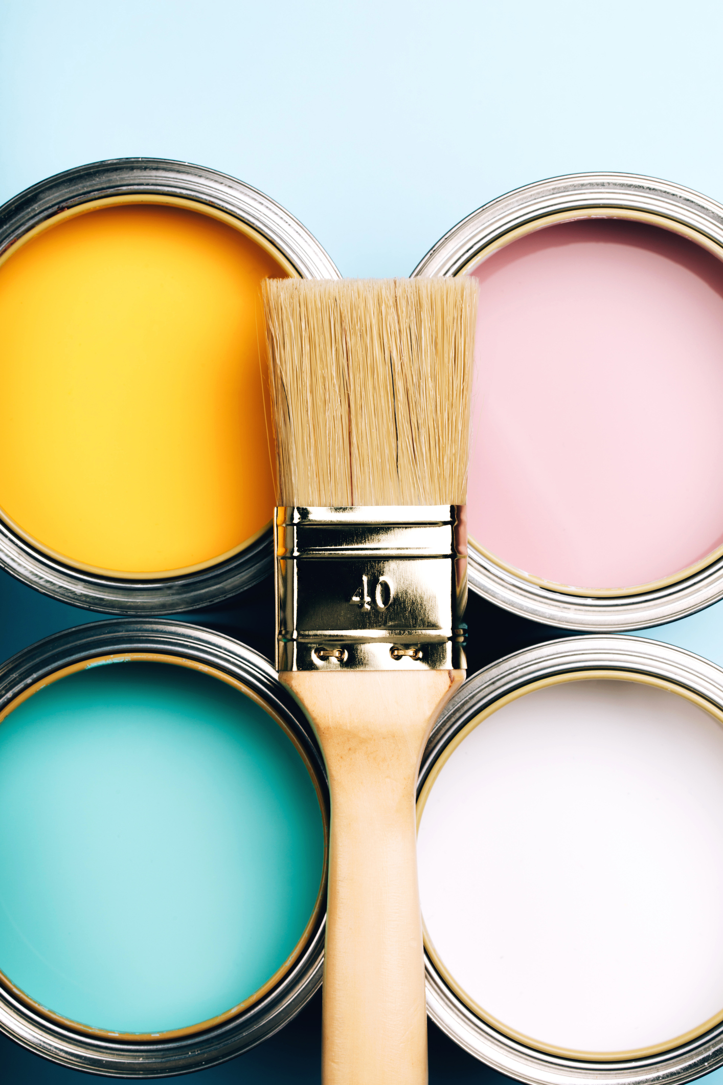 A wooden handle brush on open cans and on a blue pastel background.