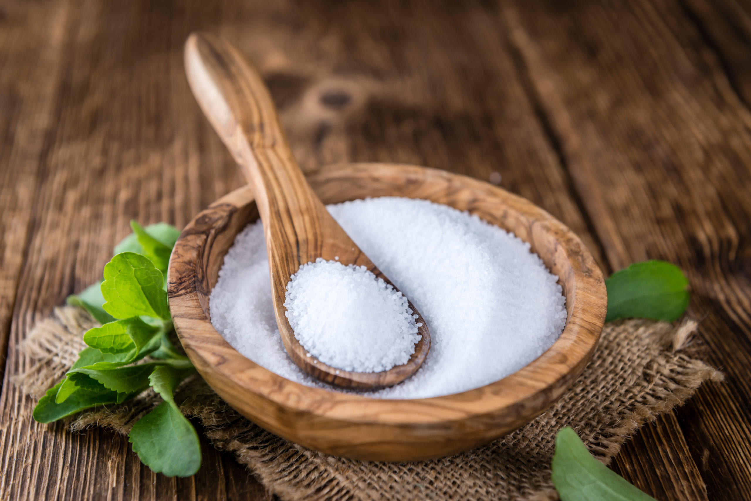 A wooden bowl of sugar with a wooden spoon in it