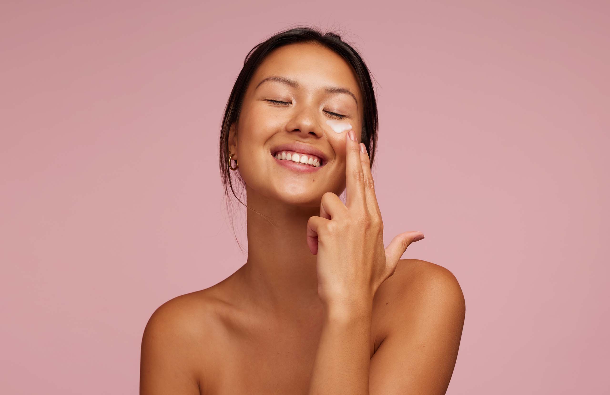 Smiling woman applying skincare under eyes