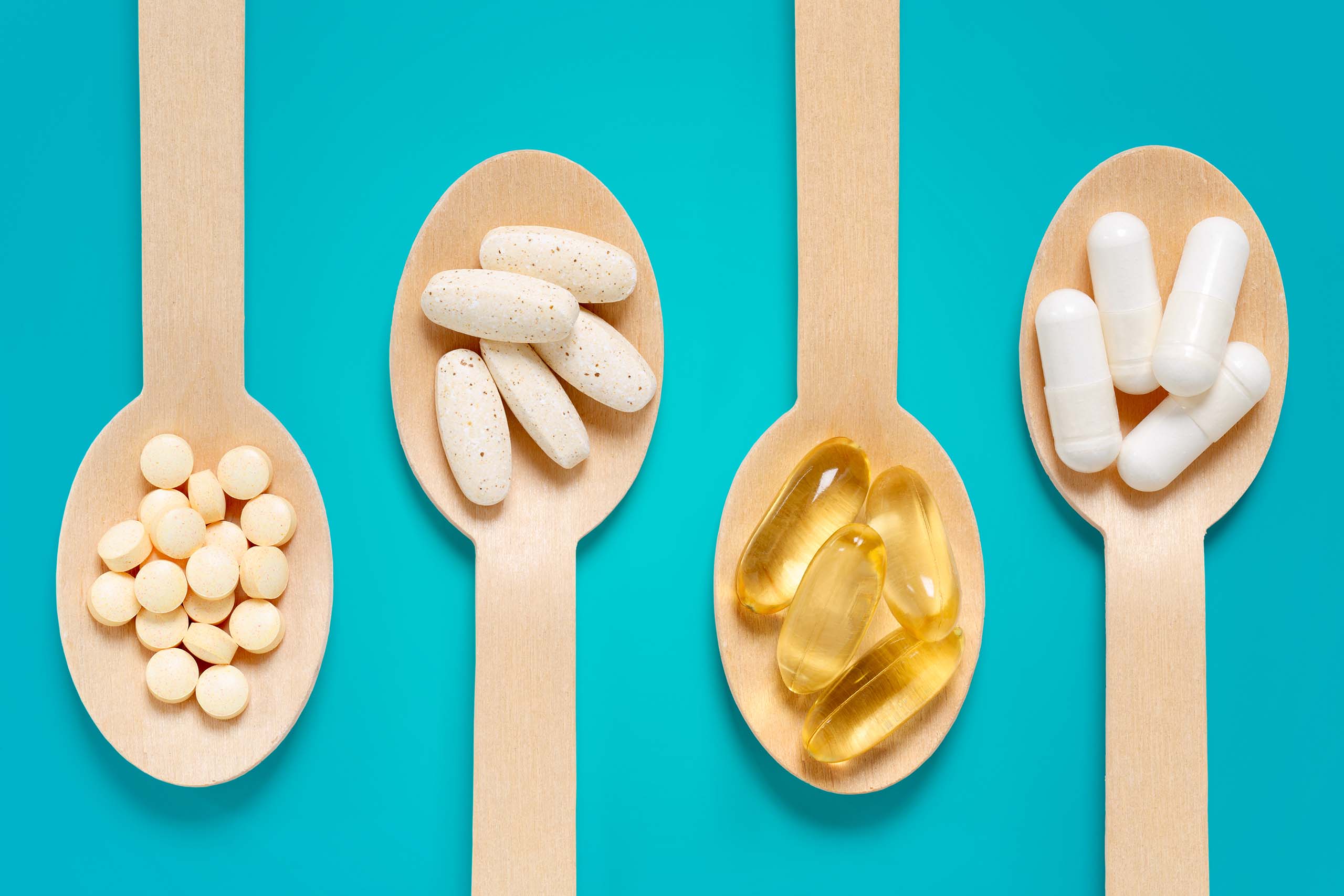 Four wooden spoons filled with different types of pills